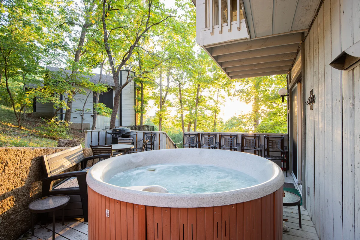 A serene exterior shot of a private deck featuring a hot tub, outdoor seating, and a backdrop of trees. The setting invites relaxation after a day of adventure, with space for families to unwind together in the tranquil natural environment.