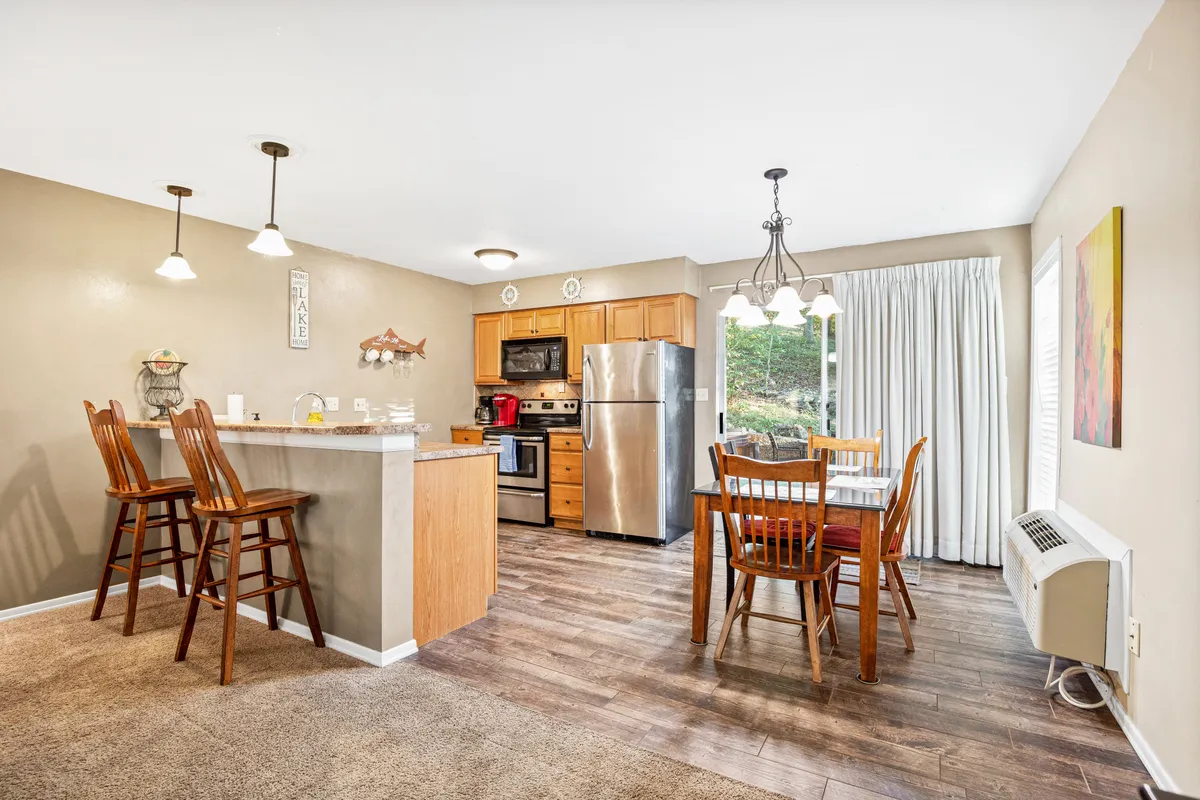 A welcoming interior scene showing a spacious kitchen island, dining table, large window letting in natural light, and modern stainless steel appliances. The space feels bright and perfect for family meals or entertaining, with a seamless transition from the kitchen to the dining area.