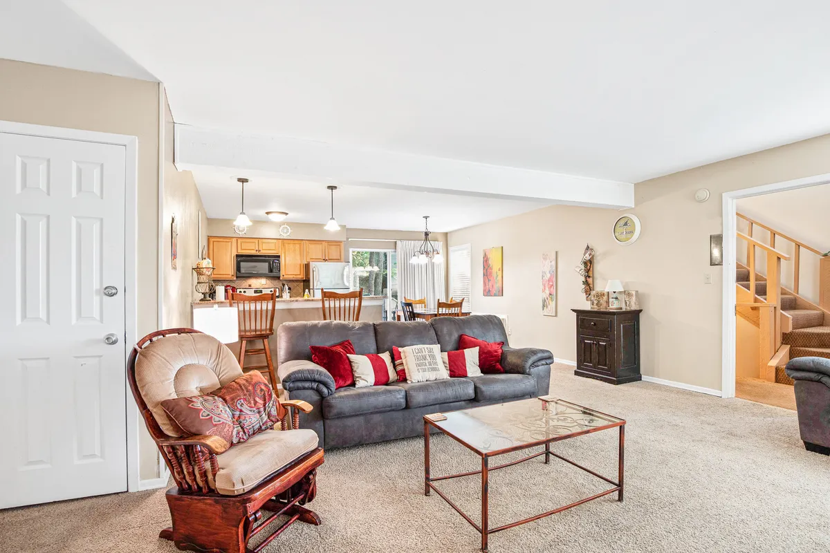 This image features a comfortable sofa and stylish armchair set in a cozy living area, with the dining area and kitchen space visible in the background. The layout showcases the connected, open-plan design, with soft lighting and warm décor inviting guests to relax or gather together.