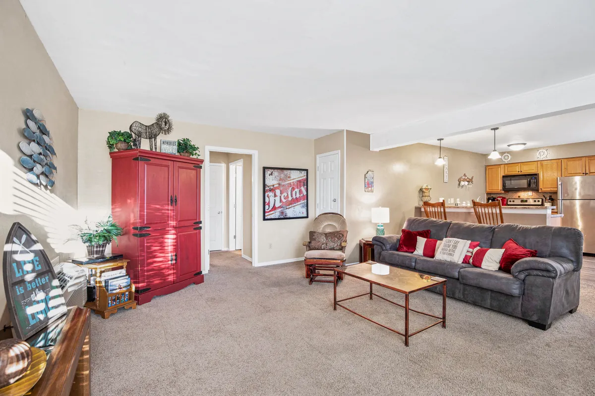 A cozy, inviting living room featuring a comfortable sofa, red armoire, coffee table, and decorative wall art. The setup encourages guests to relax, lounge, or gather for games and conversation in a warm atmosphere.